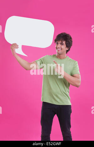 Portrait of smiling young man pointing at speech bubble over pink background Stock Photo