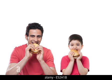 Portrait of happy father and son eating burgers over white background Stock Photo