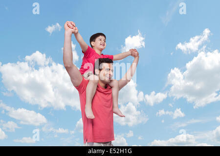 Happy father carrying son on shoulders against cloudy sky Stock Photo