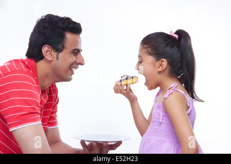 Happy father looking at daughter eating donut over white background Stock Photo