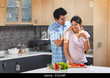 Affectionate man putting necklace on woman in kitchen Stock Photo