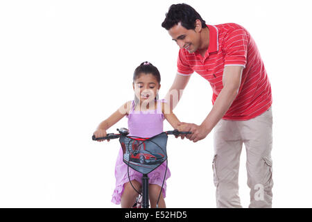 Father assisting daughter in riding bicycle over white background Stock Photo