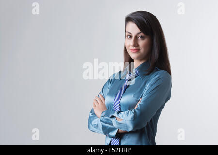 Portrait of young Indian businesswoman with arms crossed standing against gray background Stock Photo