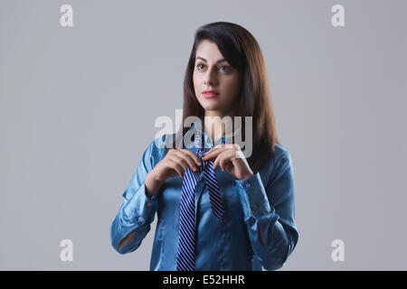 Determined businesswoman tying tie against gray background Stock Photo