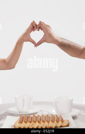Cropped image of couple making heart shape sign while having coffee against white background Stock Photo