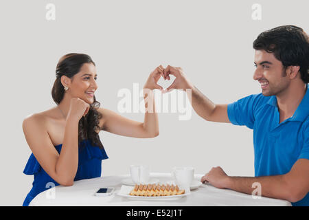 Happy young couple making heart shape sign while having coffee against white background Stock Photo