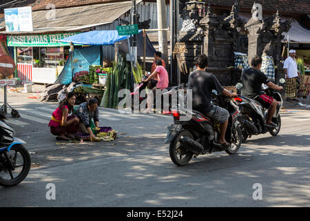 Bali, Indonesia.  Woman Placing Offerings (Canangs) at a Traffic  Intersection.  Jimbaran. Stock Photo