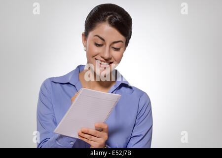 Happy Indian businesswoman writing on notebook against gray background Stock Photo