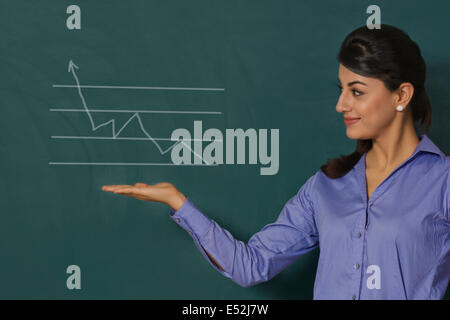 Confident young businesswoman displaying graph on green board at office Stock Photo