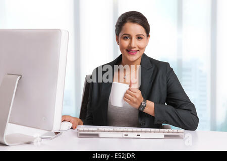 Portrait of smiling businesswoman having coffee at desk in office Stock Photo