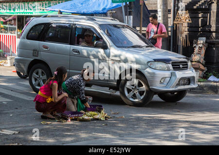 Bali, Indonesia.  Woman Placing Offerings (Canangs) at a Traffic  Intersection.  Jimbaran. Stock Photo