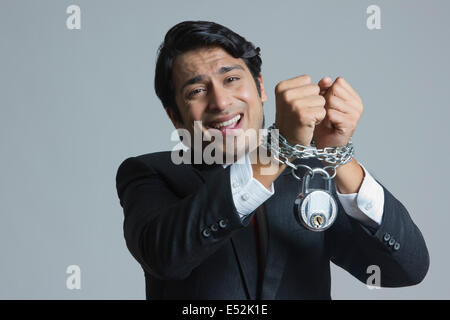 Portrait of struggling businessman's hand tied in chain over gray background Stock Photo