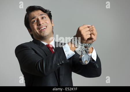 Struggling young businessman's hand tied in chain over gray background Stock Photo