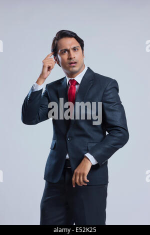 Confused businessman scratching head against gray background Stock Photo