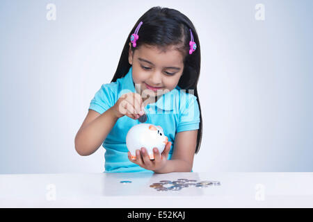 Smiling girl putting coins in piggy bank against blue background Stock Photo