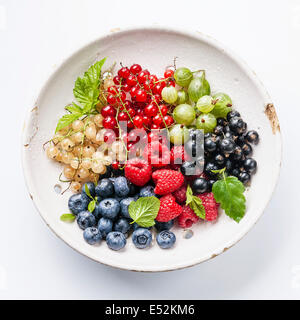 Mix of fresh berries with leaves in vintage ceramic colander on white background Stock Photo