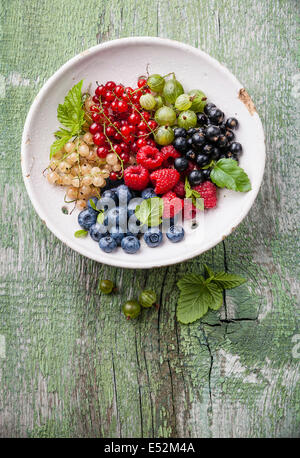 Mix of fresh berries with leaves in vintage ceramic colander on green rustic wooden background Stock Photo