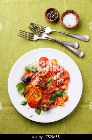 Ripe fresh colorful tomatoes salad with olive oil and balsamic vinegar on green background Stock Photo