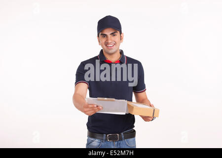 Portrait of delivery man with cardboard box and clipboard against white background Stock Photo