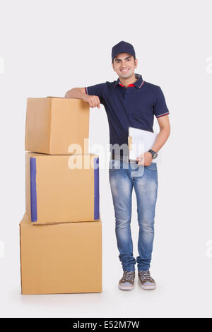 Full length portrait of smiling delivery man with stacked cardboard boxes against white background Stock Photo