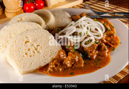 Czech traditional goulash with breaded dumpling and onion on white plate on wood table Stock Photo