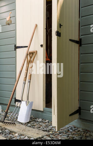 Garden fork, spade and rake, leaning against a wooden, painted shed. Stock Photo