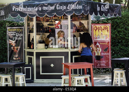 Probably the best cherry liqueur in Óbidos. Sign above the kiosk. Young lady serving cherry liqueur during a festival in Caldas da Rainha, Portugal Stock Photo