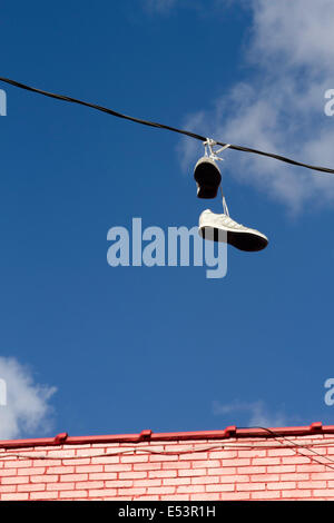 Unrecoverable shoes hanging over a wire by its tied shoelaces, thrown up there as a prank Stock Photo