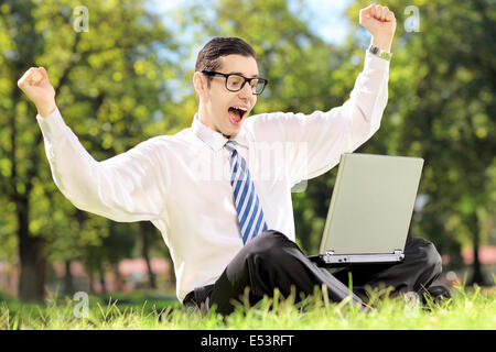 Young man cheering and watching TV on a laptop in park on a sunny day Stock Photo