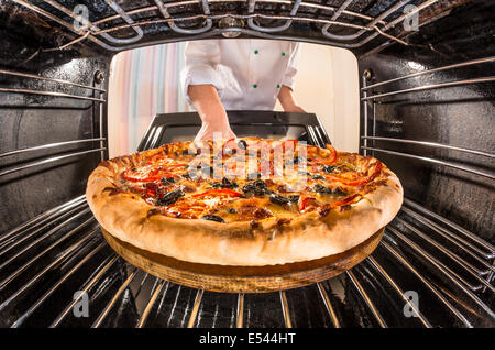 Chef prepares pizza in the oven, view from the inside of the oven. Cooking in the oven. Stock Photo