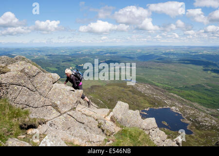 Female hiker scrambling up rocks on Carnedd Moel Siabod Daear Ddu east ridge with view down to Llyn y Foel Snowdonia National Park, Wales UK Stock Photo