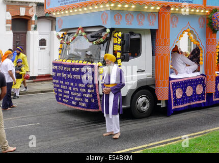 Middlesbrough, UK. 20th July, 2014. The annual Nagar Kirtan Parade celebrating Sikh culture in the North-east of England took place in Middlesbrough Cleveland UK today Sunday 20 July. The parade is led by five saffron robed men leading a float which carries the Guru Granth Sahib, the Sikh Holy Scripture.  Members of the procession are barefoot in deference to the scripture so displayed.  They are preceded by sweepers cleaning the road.  This picture shows the float carrying the Guru Granth Sahib, the Sikh Holy Scripture Credit:  Peter Jordan NE/Alamy Live News Stock Photo