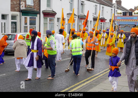 Middlesbrough, UK. 20th July, 2014. The annual Nagar Kirtan Parade celebrating Sikh culture in the North-east of England took place in Middlesbrough Cleveland UK today Sunday 20 July. The parade is led by five saffron robed men leading a float which carries the Guru Granth Sahib, the Sikh Holy Scripture.  Members of the procession are barefoot in deference to the scripture so displayed.  They are preceded by sweepers cleaning the road. This picture shows the volunteer street cleaners in front of the parade Credit:  Peter Jordan NE/Alamy Live News Stock Photo