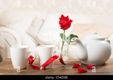 Teapot and teacups with single red rose stem Stock Photo