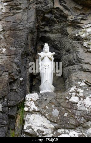 A small religious figurine of Mary and baby Jesus, dedicated to fishermen, is set in a hollowed out rock face, to look over the sea. Stock Photo