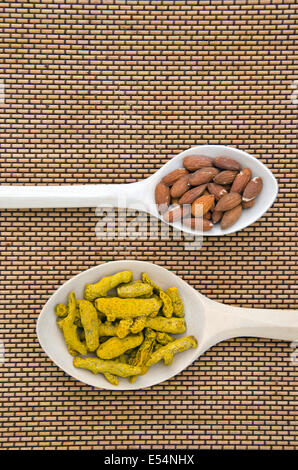 almond nuts and curcuma turmeric (Curcuma longa) dry roots in wooden spoons Stock Photo