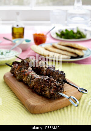 barbecued Greek Souvlaki Chicken Kebabs with Tzatziki Sauce on board in front of window with pita bread Stock Photo