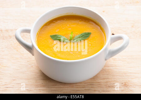 Pumpkin soup in white bowl topped with mint Stock Photo