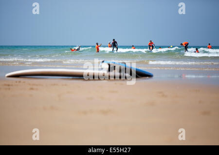 group of people having surf lessons among waves on a sand beach in Spain and surfboards in foreground blue sky in background Stock Photo