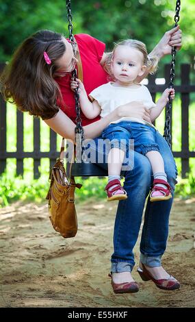 Happy mother and daughter sitting on swing Stock Photo