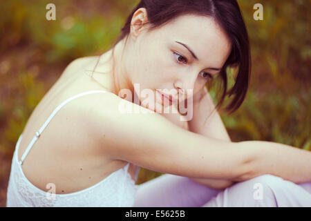 Young thoughtful woman sitting on a meadow Stock Photo