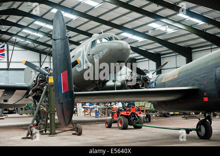Framed by the tail of a Lancaster,  Dakota combat veteran Drag-Em-Oot undergoing maintenance in the hangar at Lincolnshire Aviation Heritage Centre Stock Photo