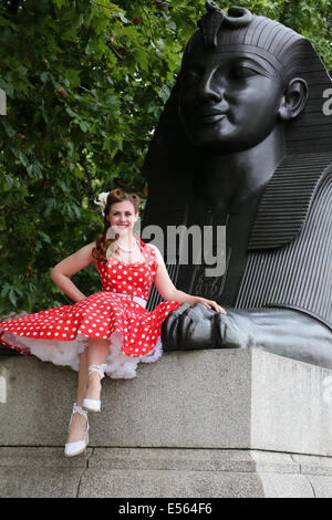 Woman in bright red polka dot dress sitting on the Sphinx on London Embankment Stock Photo