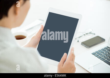 Business person holding modern digital tablet and looking on a blank screen. Stylish modern office workplace on a background. Stock Photo