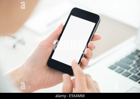 Business person holding modern smartphone and touching on a blank screen. Stylish modern office workplace on a background. Stock Photo