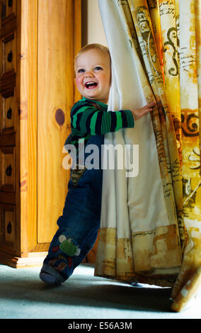 A happy little boy hiding behind curtains and smiling Stock Photo