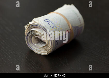 roll of UK money on a black background with a rubber band around Stock Photo