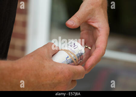 paying with cash, 2 hands and roll of money as if in payment maybe cash in hand. The cash is UK pounds sterling in a roll. Stock Photo