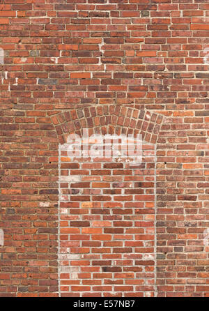 An old brick exterior wall with a window covered in newer bricks. Stock Photo
