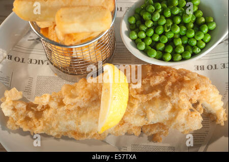 Deep fried fish (Haddock) and chips with garden peas and a segment of lemon on a fake newspaper style backing paper. Stock Photo